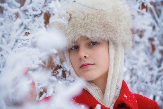 Happy teenager girl in fur hat walking in winter park