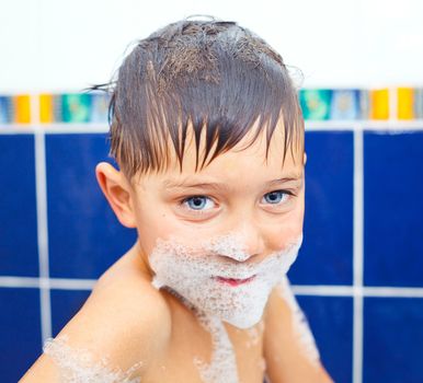 Close-up portrait of cute little boy in bathroom with foam