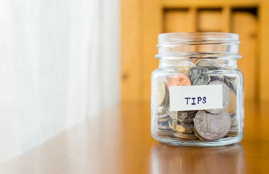 Glass bank with many world coins and  tips word or label on saving money jar