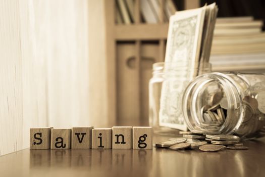 Saving word on rubber stamps place on table with coins and banknotes in money jars, sepia toning