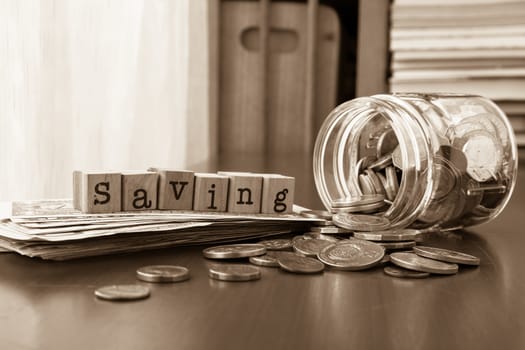 Saving word on rubber stamps place on banknotes with coins spilling out of money jars, sepia toned