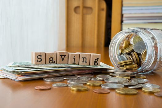 Saving word on rubber stamps place on banknotes with coins spilling out of money jars