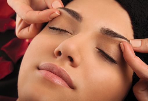 Massage the eyebrows of a young woman's face.