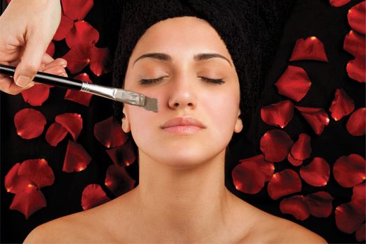 Woman during facial treatment with seaweed mask on bad with roses.