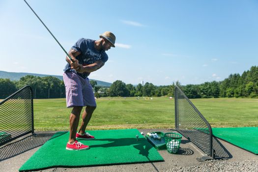 Athletic golfer swinging at the driving range dressed in casual attire.