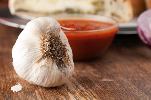 Garlic bulb closeup with tomato sauce in the background.  Shallow depth of field.