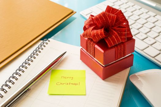 Red gift box and sticky note with christmas greeting message on office table