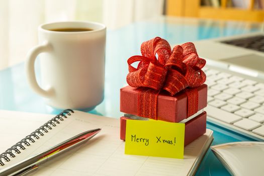 Red gift box and paper note with Merry xmas message on office table, concept to christmas greeting and holiday season