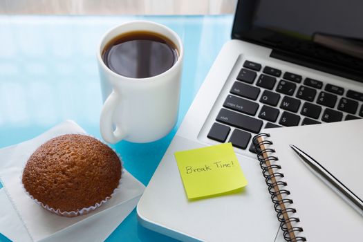 Coffee break, cupcake  and notebook place on laptop with sticky note message : Break Time, A break at work concept