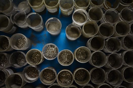 Top view of small plastic containers with various sized manganese flake grains. Blue background.