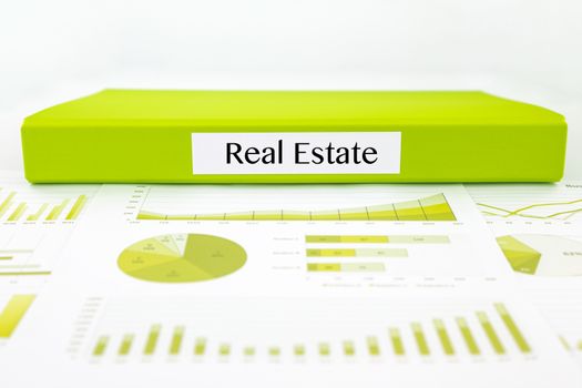 Green document binder with Real Estate word place on graphs analysis and investment reports