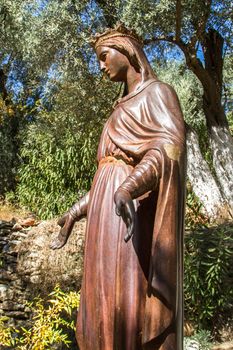 Side view of bronze statue of holy Virgin Mary in natural place.