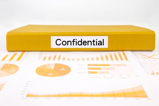 Yellow document binder with Confidential word place on graph analysis, charts and undisclosed reports