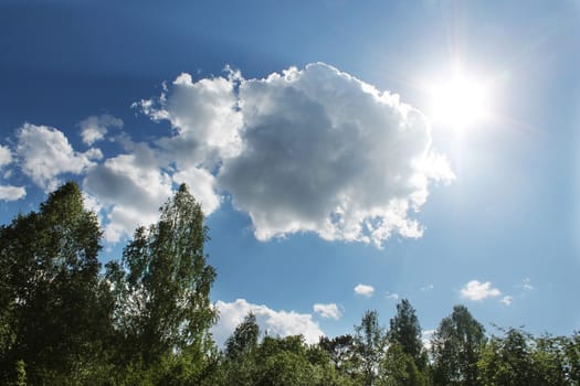 A bright summer sun in the blue sky with clouds