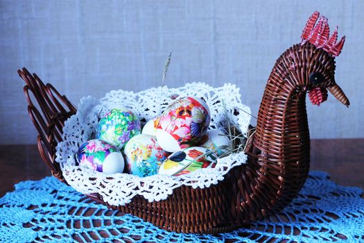 Decorative wicker vase in the form of chicken with Easter eggs inside on lacy napkin