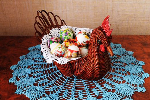 Decorative wicker vase in the form of chicken with Easter eggs inside on lacy napkin