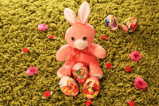 Easter eggs with pink toy rabbit placed on green synthetic grass with flowers