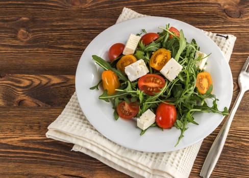 light salad of arugula, tomatoes and feta cheese on a wooden background