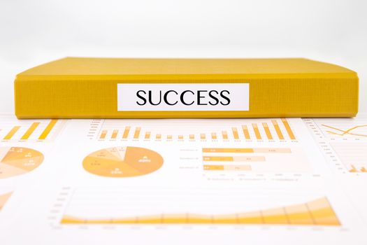 Yellow document binder with success word place on graphs, charts and business reports
