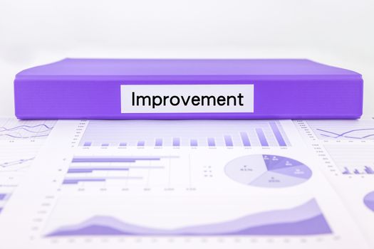 Purple document binder with Improvement word place on assessment document, graph analysis and education reports