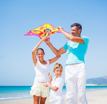 Summer vacation - Father with is two kids flying kite beach outdoor.