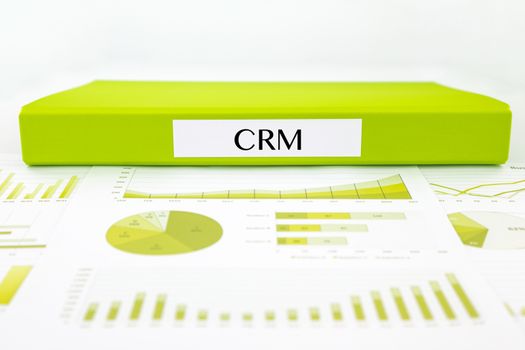 Green document binder with CRM  customer relationship management word place on graph analysis and business reports