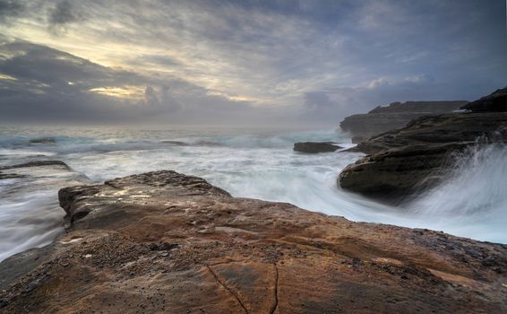Moody sunrise and wild waves lashing the coast at Little Bay NSW Australia.