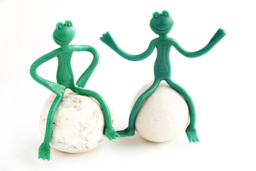 Two green frogs of plastic sitting on the stone.