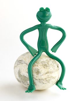 Green frog made of plastic sitting on the stone.