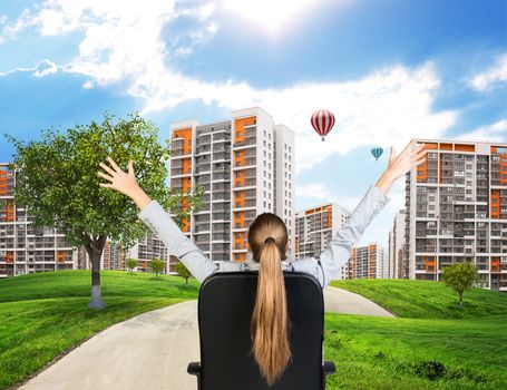 Businesswoman sitting on office chair with her hands outstretched. Green hills with buildings and sky as backdrop