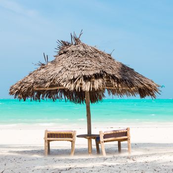 Two wooden dack chairs and umbrella on stunning tropical beach. Turquoise blue lagoon of Paje beach, Zanzibar, Tanzania.