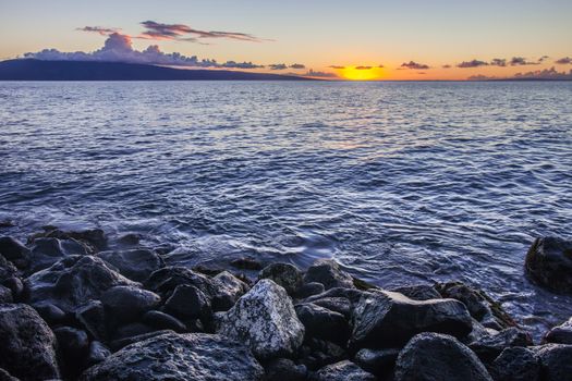 Beautiful Maui sunset with water on shore rocks