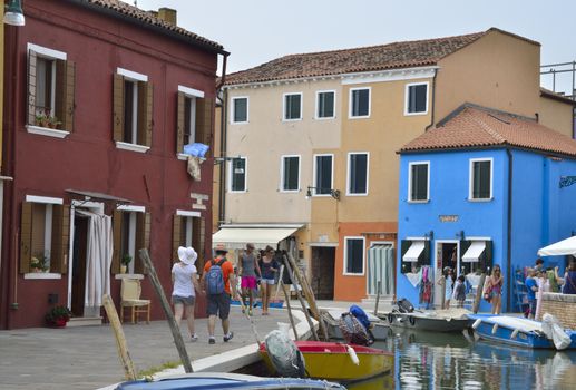 Tourists walking by a way along a small canal in Burano, a colorful island of Venice, Italy