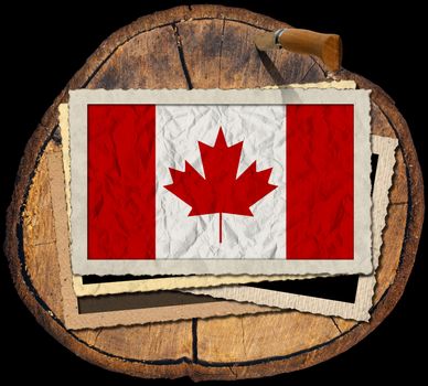 Flag of Canada in a old photo frame on a section of tree trunk isolated on black background