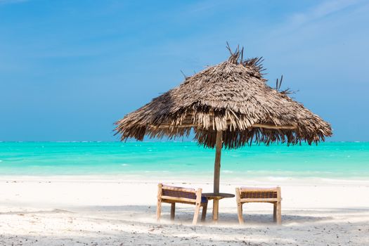 Two wooden dack chairs and umbrella on stunning tropical beach. Turquoise blue lagoon of Paje beach, Zanzibar, Tanzania.