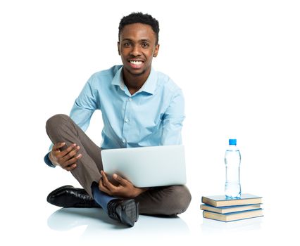 Happy african american college student with laptop, books and bottle of water sitting on white background