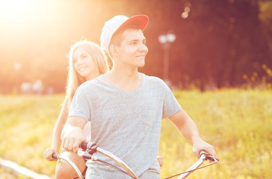 Happy couple - young man and woman riding a bicycle in the park outdoors