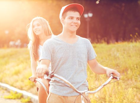 Happy couple - young man and woman riding a bicycle in the park outdoors