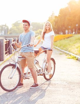 Happy couple - young man and woman riding a bicycle in the park outdoors