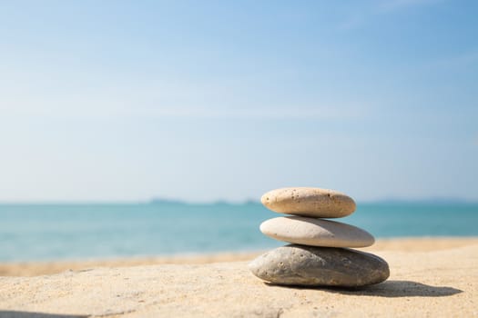 Stones balance, pebbles stack on the sand beach with shadow on right side , beautiful sea view during daytime on a sunny day with blue sky on background