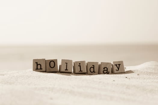 Holiday word on wood rubber stamps stack on the sand beach for break and vacation concept, ocean view on background, sepia tone image