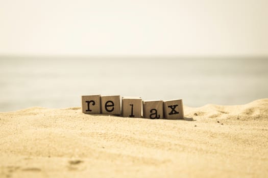Relax word on wood rubber stamps stack on the sand beach for break and vacation concept, sea view on background, retro style image
