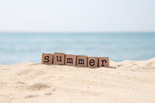 Summer word on wood rubber stamps stack on the sand beach for holiday season concepts, beautiful blue sea view during daytime on a sunny day on background