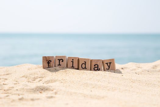 Friday word on wood rubber stamps stack on sand beach with beautiful blue sea view on background, day and time concepts