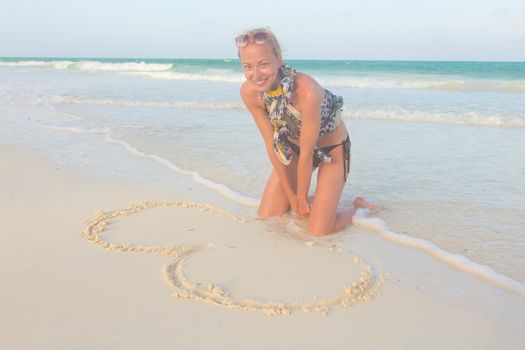 Beautiful woman drawing a heart in the sand on the beach.