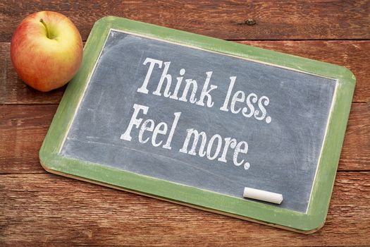 Think less. Feel more.  Motivational words on a slate blackboard against red barn wood