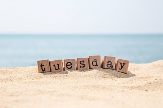 Tuesday word on wood rubber stamps stack on seaside with beautiful blue sea view on background, day and time concepts