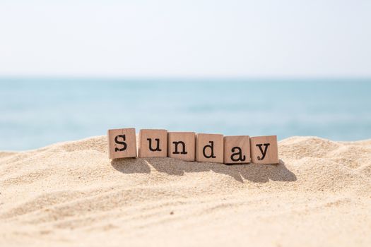Sunday word on wood rubber stamps stack on beach with beautiful blue sea view on background, day and time concepts