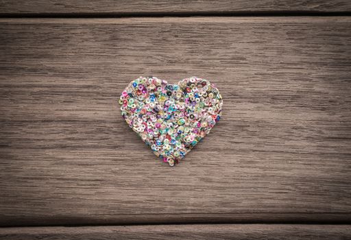 Love heart shape from colorful glitter place in the middle of wood background with vignette, anniversary and valentine's day symbol