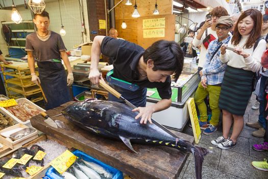 Osaka, Japan - Oct 26: People watching the cutting of a giant tuna in a seafood store in Kuromon Market in Osaka, Japan on Oct 26, 2014.